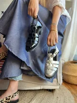 Sandalias de cuero con plataforma y múltiples tiras horizontales. Un par es de color negro charol y el otro plateado.