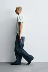 Pantalón de jeans de algodón, corte baggy fit, tiro medio, con efecto lavado en tonos grises y verdes. Presenta cinco bolsillos y cierre frontal con cremallera y botón.