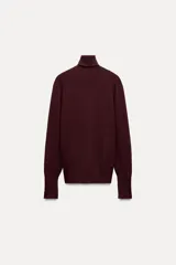 Jersey negro de punto liso con cuello alto, manga larga y detalle de botones dorados en los puños.