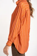 Camisa oversize color ladrillo con rayas verticales blancas y rosadas, de mangas largas y botones de madera.