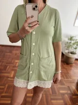 Camisola verde con botones frontales, mangas cortas, dos bolsillos y detalle de encaje blanco en el ruedo.
