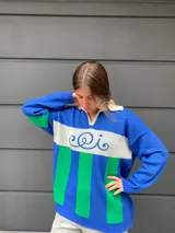 Sweater de punto azul con rayas verticales verdes y banda horizontal blanca con bordado en el pecho.