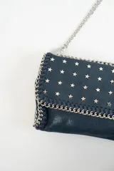 Cartera bandolera azul con tachas plateadas en forma de estrella, correa de cadena plateada y asa corta de cuero.
