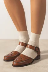 Zapato marrón de cuero vacuno trenzado a mano, con correa al tobillo con hebilla negra y suela de cuero.