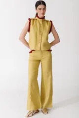 Blusa color mostaza sin mangas, con cuello alto y detalle de volados rojos en cuello, sisas y ruedo. Cierre frontal con botones.