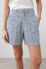 Bermuda de tiro alto con estampado de rayas verticales azules y blancas, con bolsillos laterales y cierre frontal con botón y cremallera.
