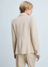 Blazer color beige con cuello de pico con solapa, hombros estructurados, cierre de botón en la parte delantera y dos bolsillos de ribete en la parte delantera.