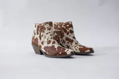 Botas texanas de caña corta con estampado animal print de vaca en tonos marrón y blanco.