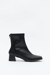 Bota corta de caña elástica color negro, con puntera cuadrada y taco geométrico de altura media. Presenta cierre de cremallera en la parte trasera.