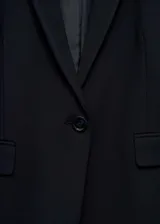 Blazer negro con cuello de pico y solapa, cierre de botón frontal, manga larga con puños abotonados, diseño recto y dos bolsillos de solapa delanteros.