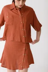 Camisa corta de manga corta color rojo, con doble cartera diagonal con botones de madera, cuello clásico y botamangas marcados. Tiene un bolsillo con aplique de crochet hecho a mano con forma de frutilla.