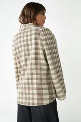 Saco corto de tela a cuadros color beige y marrón, con cuello solapa, manga larga y cierre frontal con un botón. Tiene un bolsillo de parche en el frente.