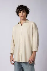 Camisa de lino color beige, de corte recto, con cuello clásico, cierre frontal con botones y mangas largas con puños abotonados.