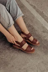 Sandalias de cuero marrón con tiras tejidas a mano y costuras a la vista, con base plana.