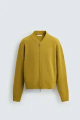 Chaqueta color mostaza de punto con cuello mao, corte relaxed fit, manga larga, bolsillos laterales y cierre frontal con cremallera.