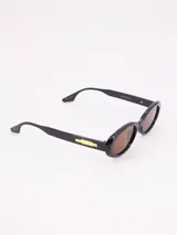 Lentes de sol con montura ovalada negra y cristales marrones.