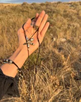 Collar artesanal con dije de flor plateada, realizado con hilo de seda natural teñido a mano.