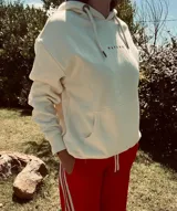 Hoodie color crema con capucha y cordón ajustable. Estampado en la espalda con un paisaje de montañas, árboles y un oso.