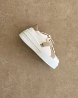 Zapatillas deportivas urbanas con capellada negra, detalles en beige y suela blanca.