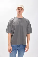 Camiseta manga corta gris oscuro con estampa de un paisaje marino y texto en color blanco. Corte amplio y recto, con proporciones cuadradas.