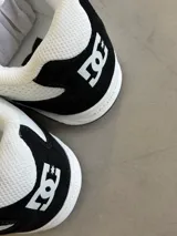 Championes DC Manteca 4, color blanco con detalles en negro. Presentan una parte superior de malla y cuero sintético, con el logo de DC en la lengüeta y el lateral. Cuentan con cordones blancos y una suela de goma.