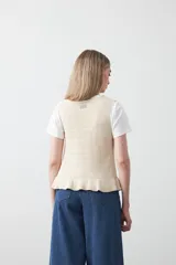 Chaleco tejido de punto color beige con trama texturada y diseño liviano. Presenta cuello a la base, silueta recta y cierre frontal mediante tres lazos delicados.