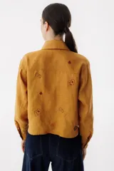 Camisa azul de lino con cuello clásico, manga larga y cierre frontal con botones. Presenta bordados de dados, cartas y el nombre de la marca.