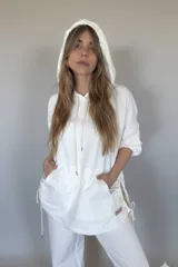 Canguro oversize color blanco, con capucha, cordones ajustables, mangas 3/4 con puños elásticos, bolsillos laterales y ruedo irregular con cordones ajustables.