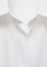 Camisa blanca oversize de algodón con cuello camisero, manga larga con puños abotonados, bolsillo de parche en el pecho y cierre frontal con botones.