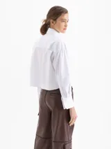 Camisa blanca de poplin de algodón con fit cómodo y largo que cubre hasta debajo de la cintura. Presenta botones ocultos en cartera y puños, y punteras de níquel en el cuello.