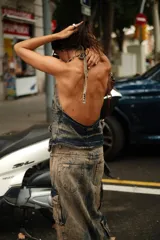 Chaleco tipo top de denim con efecto ahumado (lavado ácido/tie-dye en tonos azules y morados). Presenta escote marcado, bolsillos tipo cargo frontales con argollas metálicas en color bronce y cordones ajustables en el frente.