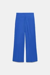 Pantalón negro de tiro alto con corte palazzo, bolsillos laterales y pliegues frontales. Cierre frontal con cremallera y botón.