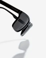 Lentes de sol Hawkers unisex con montura rectangular negra y lentes grises.