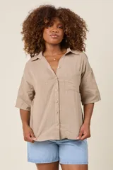 Camisa color beige claro, de corte clásico, con cuello, botones frontales, bolsillo en el pecho y mangas tres cuartos con presilla para sujetar.