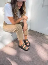 Sandalias de cuero color marrón con dos tiras anchas con hebillas metálicas y ojalillos.