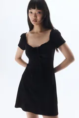 Vestido corto negro de punto acanalado con escote corazón ribeteado en encaje y cordón para ajustar en el centro del busto. Modelo de manga corta con cuerpo entallado, copas preformadas y pollera con vuelo.