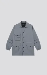 Campera gris con broches en el delantero, forrada con red, múltiples bolsillos con detalles en réflex y puños elásticos en las mangas. Confeccionada en textil liviano 100% poliéster y calce oversize.