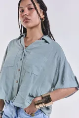 Camisa verde agua con cuello clásico, cierre frontal con botones, mangas cortas con dobladillo y dos bolsillos de parche en el pecho.