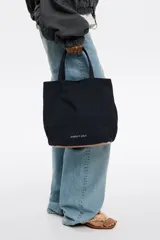 Bolso de mano Bimba y Lola modelo Chihuahua L, color marrón, con doble asa de mano y asa bandolera de tejido. Cierre con botón de presión, logo metálico y acabados plateados.