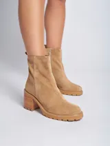 Bota corta de gamuza color marrón, con taco cuadrado de madera y suela track. Presenta un tirador en la parte posterior. Confeccionada 100% en cuero genuino.