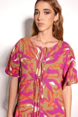 Vestido corto con estampado abstracto en tonos marrones, fucsias, naranjas y blancos. Tiene escote con abertura y lazos ajustables, mangas cortas con leve volumen y corte holgado.