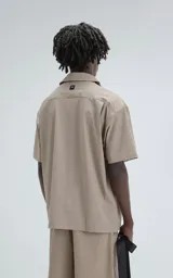 Camisa beige de manga corta, estilo técnica, confeccionada en microfibra liviana. Con doble bolsillo frontal y broches en lugar de botones.