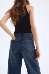 Pantalón jean azul de denim de algodón levemente elástico, corte ancho, tiro alto, largo tobillero y cinco bolsillos.