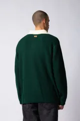 Sweater de punto verde con cuello polo color crema y bordado frontal con texto en blanco.