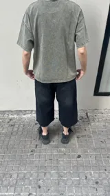 Bermuda de jean negra con lavado oscuro, corte ancho (baggy) y largo hasta la rodilla (3/4). Presenta un dobladillo deshilachado en el ruedo y cierre frontal con botón y cremallera.