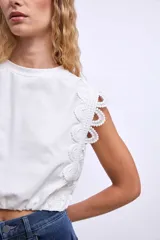 Remera blanca de algodón con mangas cortas y detalle de encaje calado en los hombros.