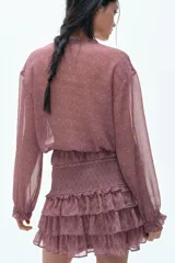 Blusa rosa con estampado floral, cuello con volados y escote en V con tiras finas para atar. Modelo de manga larga con hombros caídos y fruncido elástico con ribete de volados en puños y bajo.