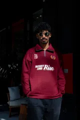 Buzo de algodón color bordó, estilo universitario, con cierre medio frontal y cuello alto. Estampado frontal con el texto "Since 19" y un ancla con laureles en amarillo y blanco.