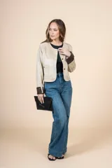 Chaqueta corta color beige, con cuello redondo, cierre frontal con botones dorados, bolsillos de parche y puños en contraste color marrón.