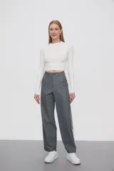 Pantalón gris de calce ancho y tiro alto, con bolsillos laterales y apliques de dos líneas blancas verticales en los laterales.